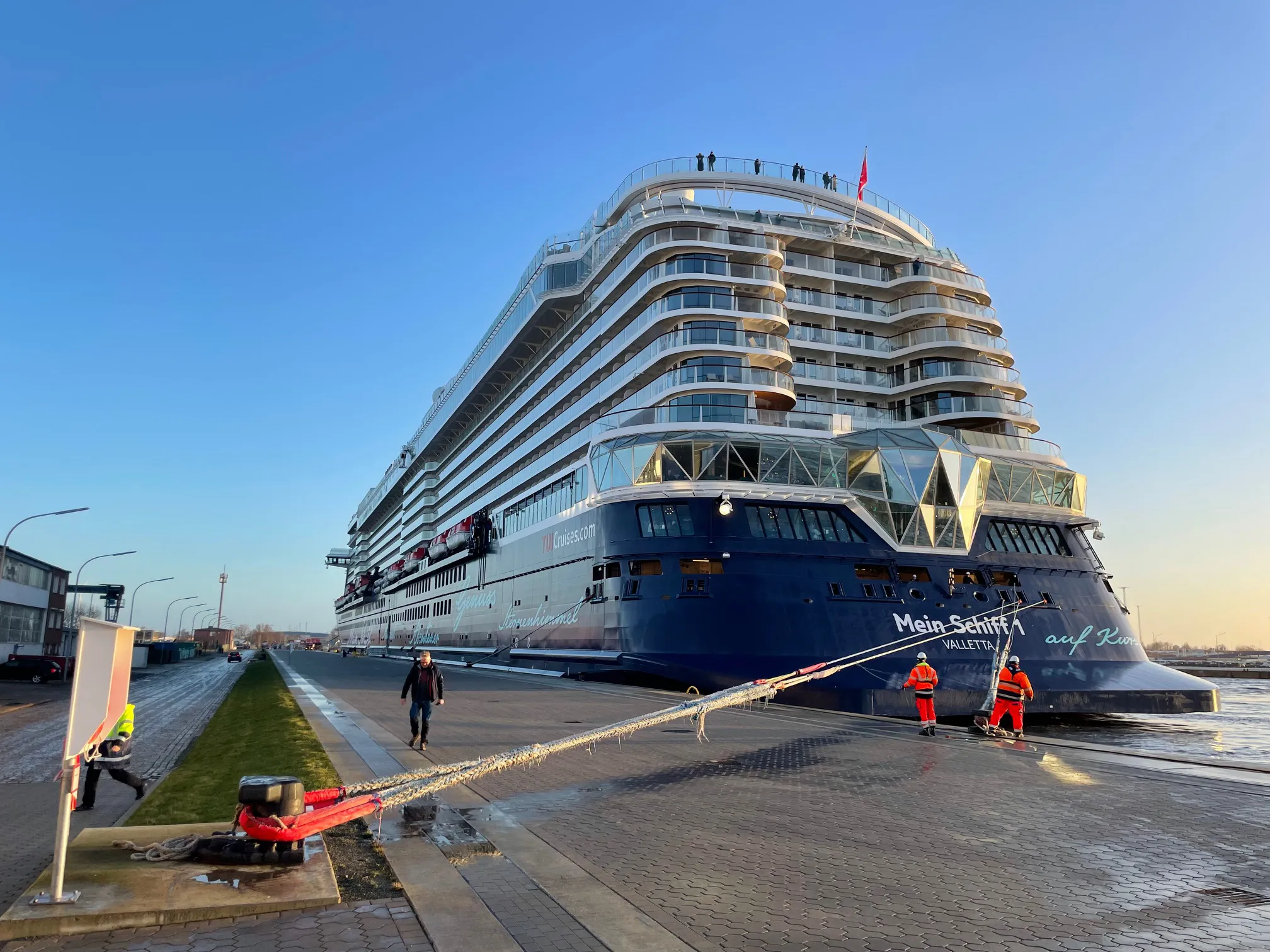 Kreuzfahrtschiff „Mein Schiff“ festgemacht am Kai, Menschen arbeiten am Ufer.